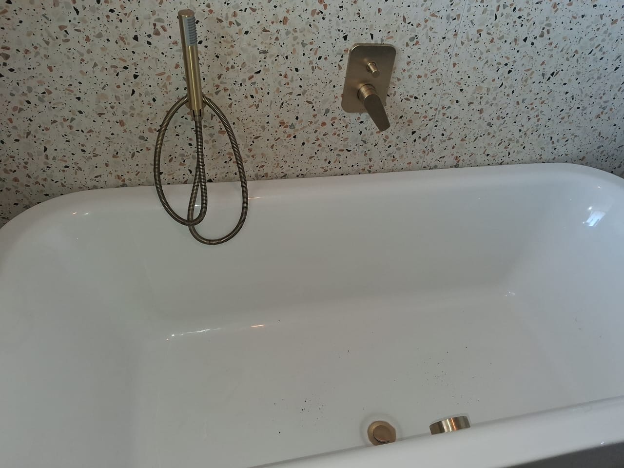 Freestanding bath with brushed-gold mixer on terrazzo wall