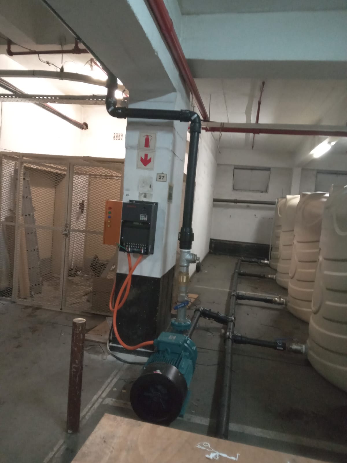 Commercial plant room with beige water tanks, teal pump and control panel